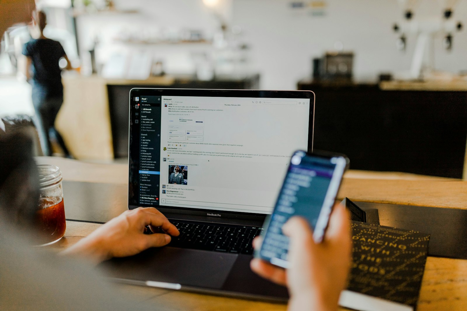 A person using a smartphone beside a laptop